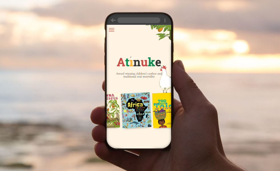 Smartphone displaying Atinuke author page, innovative web project showcasing African childrens books on a Welsh beach at sunset.