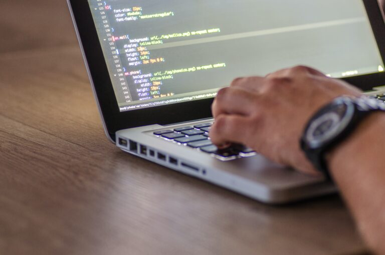Web developer in Wales coding on laptop with HTML CSS visible on screen, enhancing modern web design.